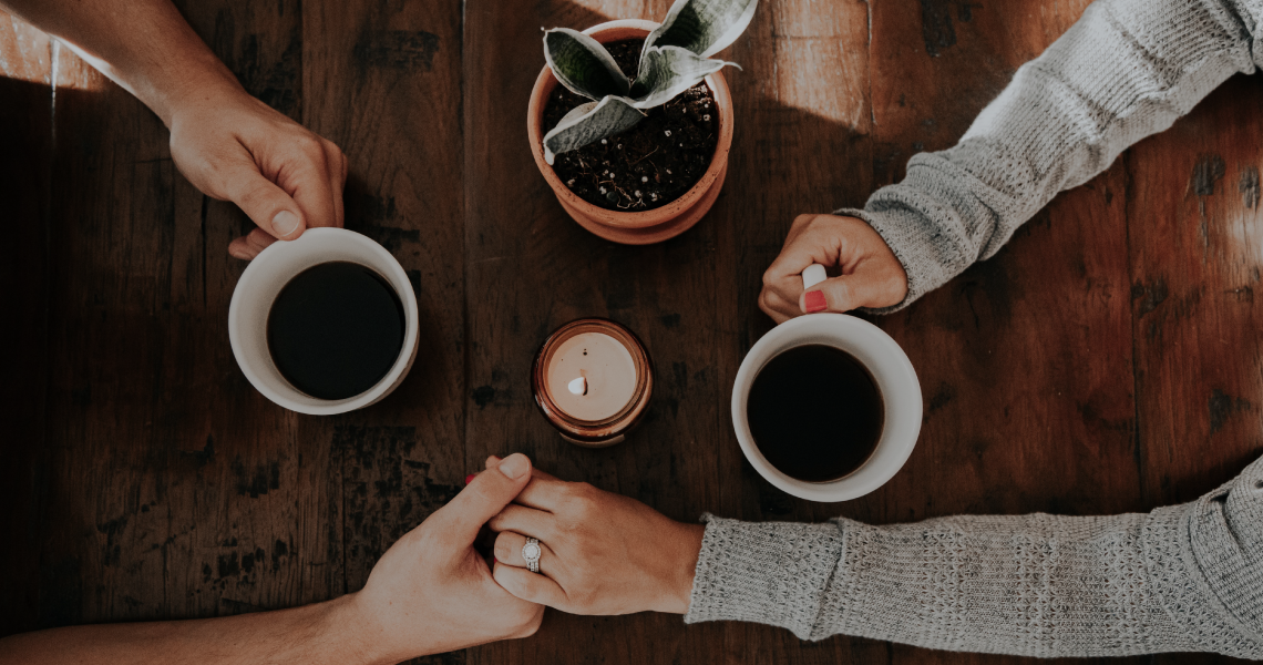 two people holding hands while sitting at a table with cups of coffee