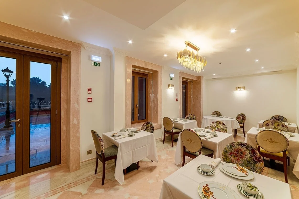 Elegant dining room with tables set for breakfast, featuring floral chairs and a chandelier. Marmoris Hotels
