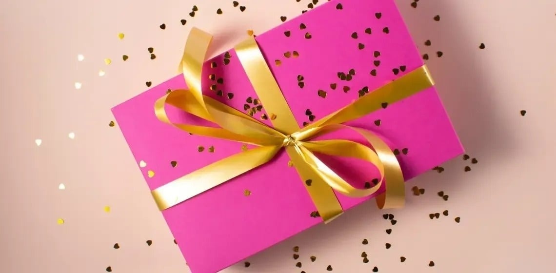 a pink gift box with a gold ribbon and bow