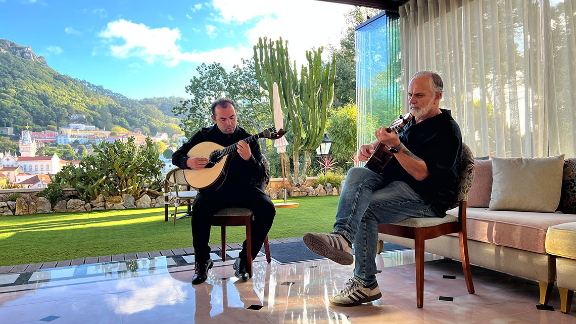 Dois músicos tocam guitarra em terraço com vista para vila Marmoris: Corporative.