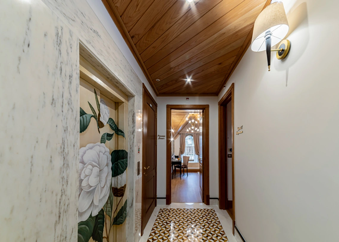 Elegant hotel hallway with ornate elevator, wood ceiling, and ornate sconce Marmoris Hotels