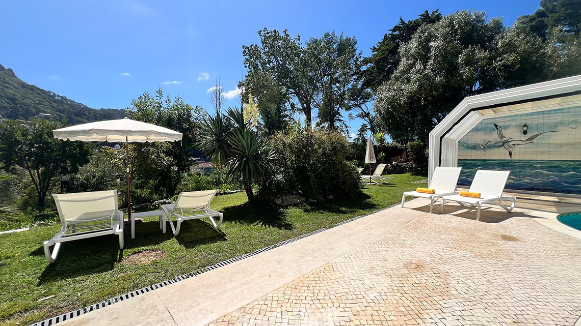 Tadeiras brancas com toalhas laranjas em frente a uma piscina com mosaico de pássaros Marmoris: Corporative.
