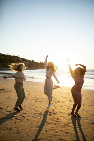 tres mujeres saltan en la playa al atardecer