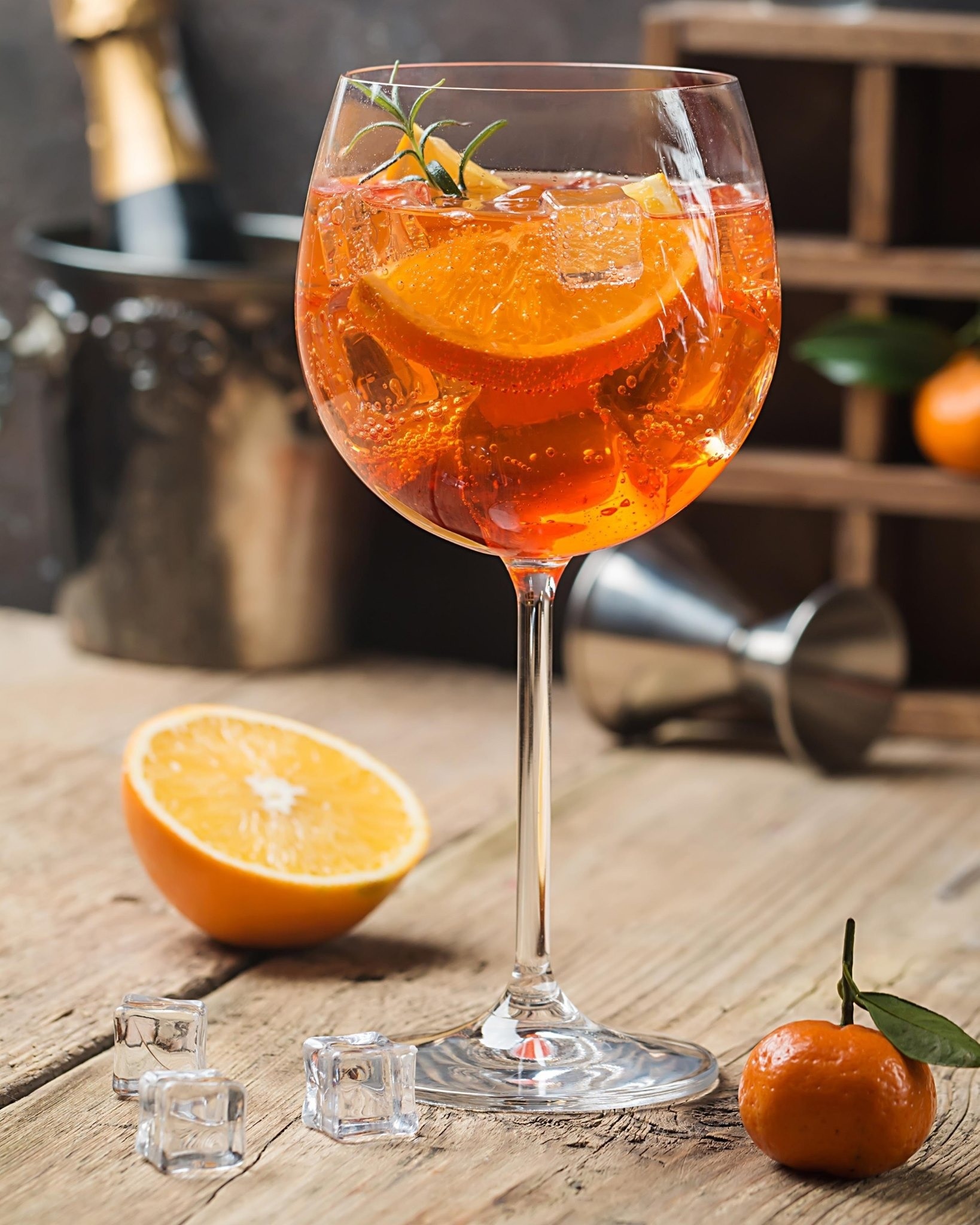 un verre de boisson orange avec des cubes de glace et une tranche d' orange sur une table en bois