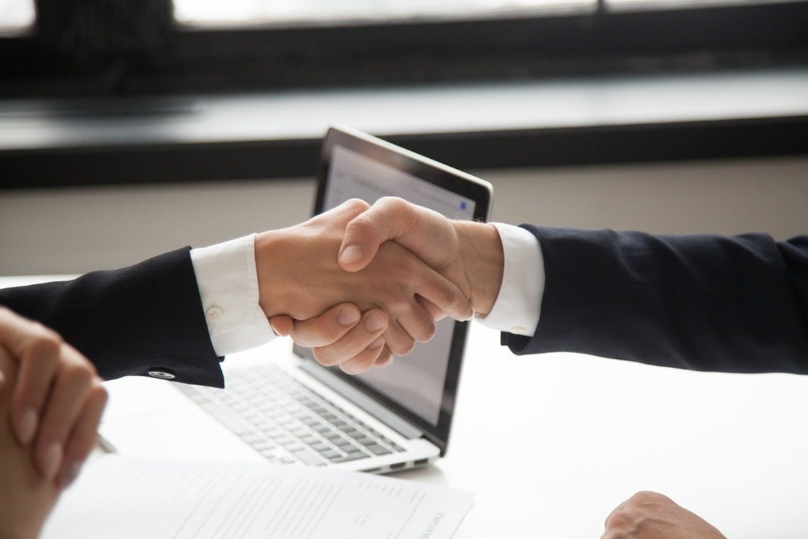 two people shaking hands in front of a laptop