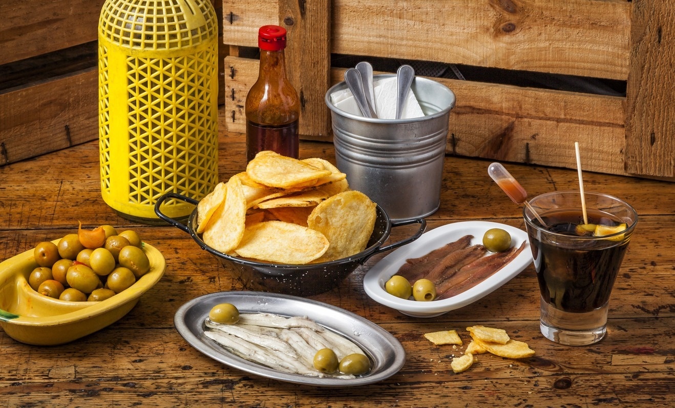 una mesa de madera llena de comida incluyendo patatas fritas y aceitunas