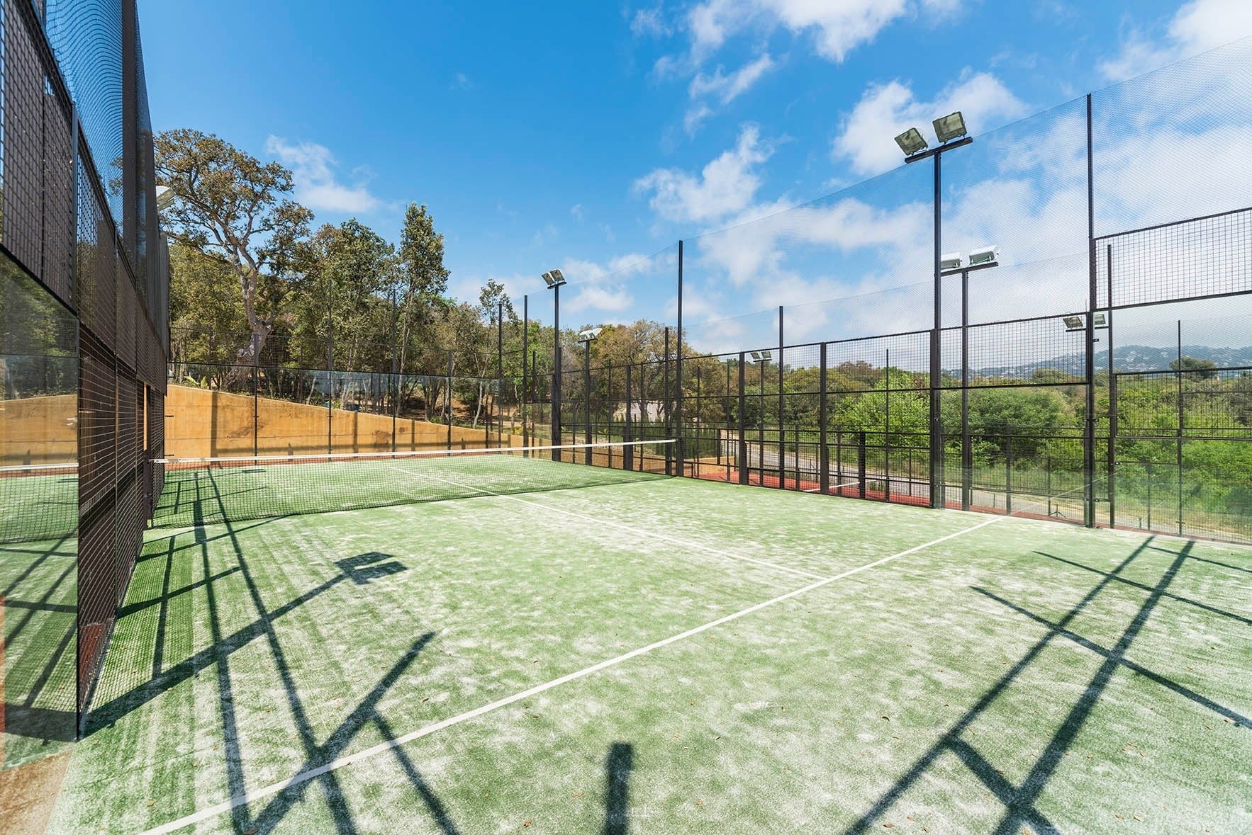 ein Tennisplatz mit einem schwarzen Zaun umgeben von Bäumen