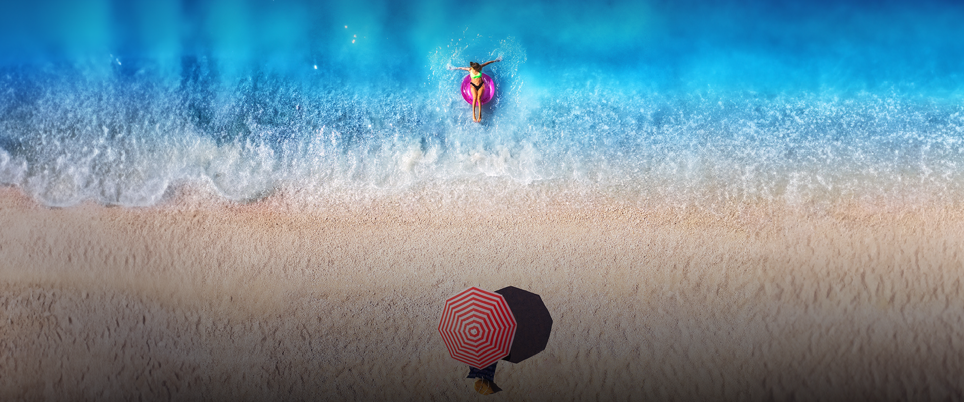 una mujer flota en un flotador en el océano mientras sostiene un paraguas a rayas rojas y blancas