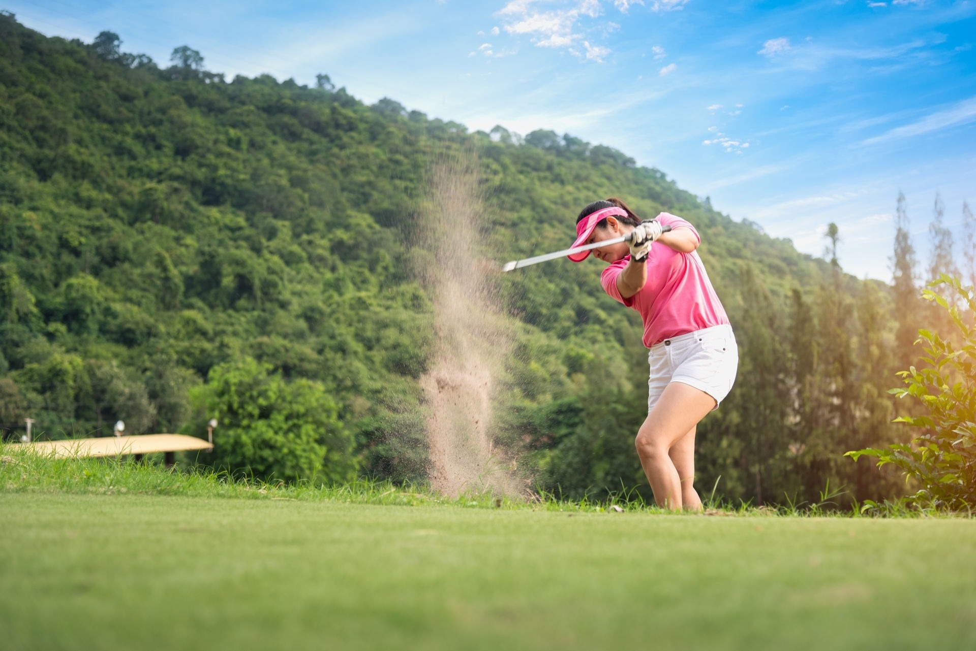 eine Frau spielt Golf und schlägt den Ball aus dem Sand