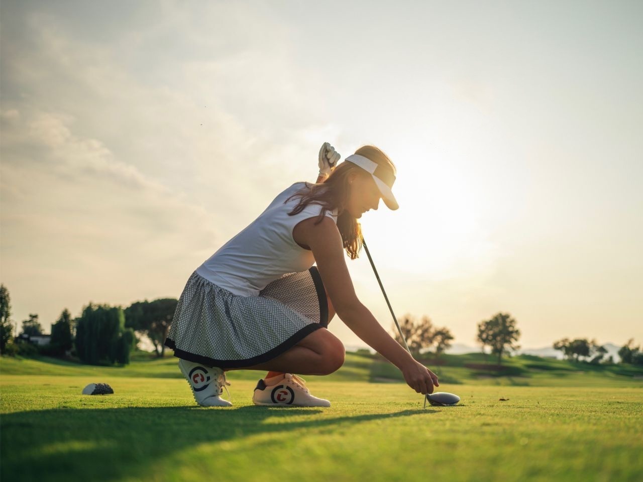 eine Frau kniet auf einem Golfplatz und hält einen Golfschläger