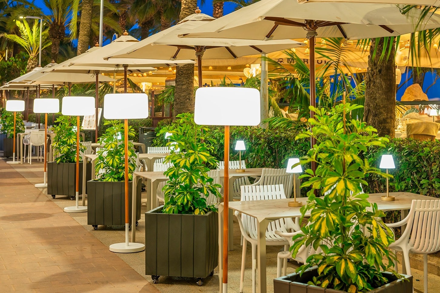 una fila de mesas y sillas en un restaurante con sombrillas y lámparas