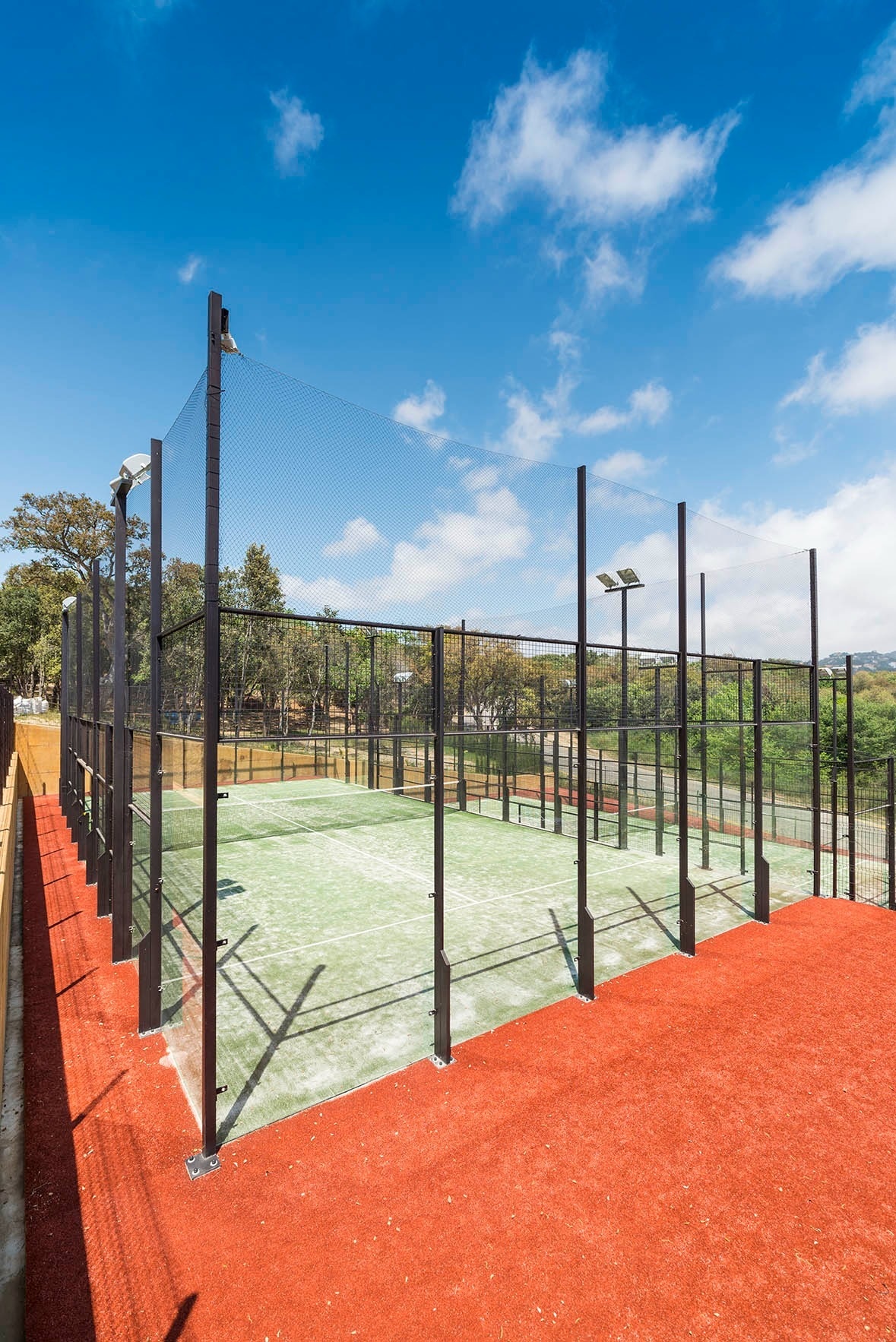 una pista de padel coberta d' herbe vermella i una cerca negra