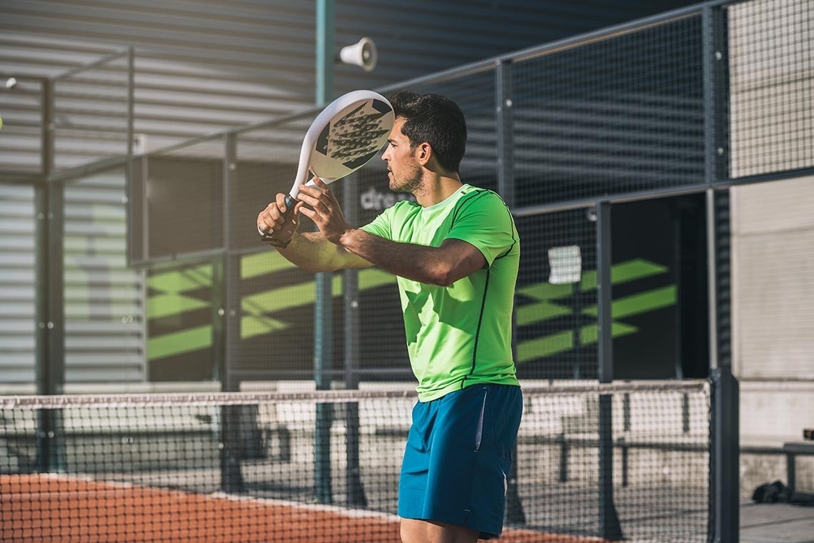 a man in a green shirt is holding a paddle on a tennis court