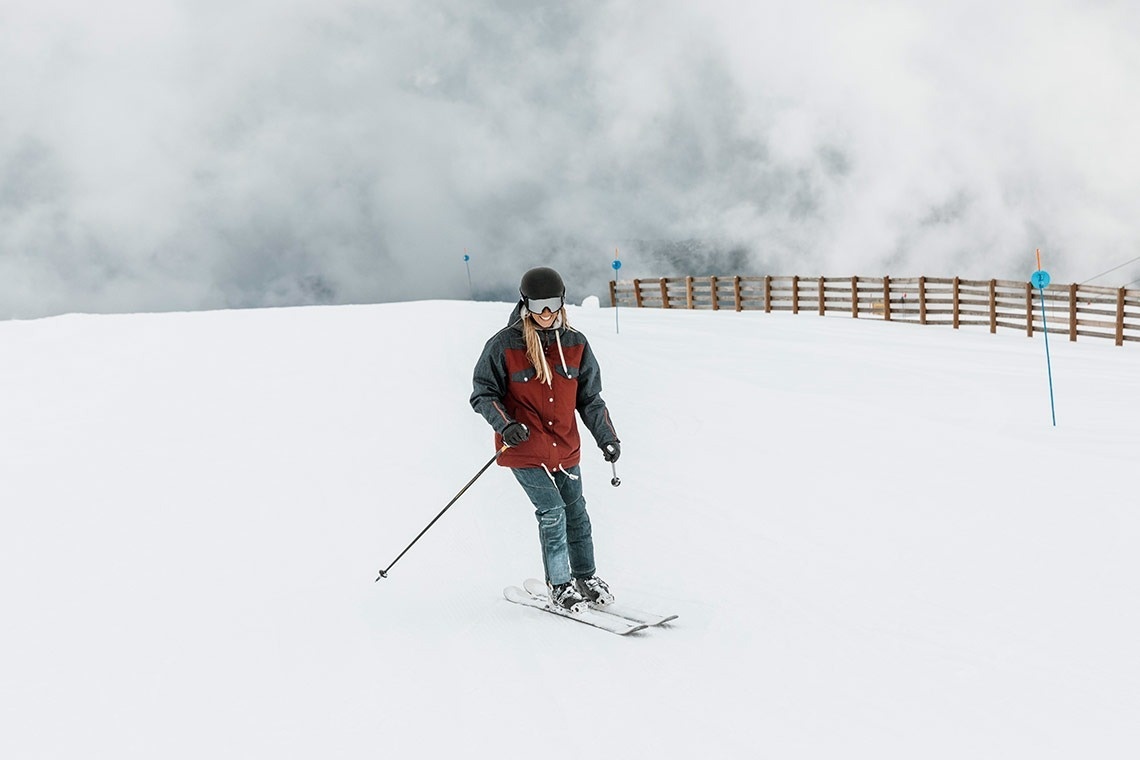 a person skiing down a snowy slope with a fence in the background