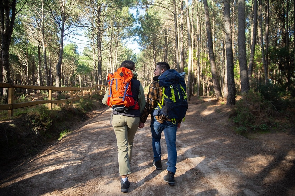 un hombre y una mujer con mochilas caminan por un sendero forestal