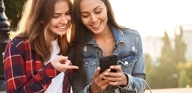 two young women are looking at a cell phone together .