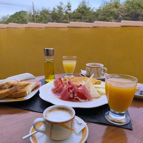 una mesa con un plato de jamón y queso junto a una taza de café y un vaso de zumo de naranja