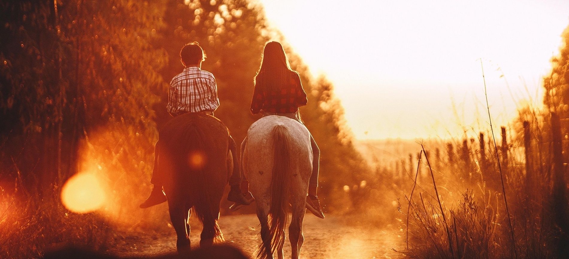 un hombre y una mujer montan a caballo por un camino polvoriento al atardecer