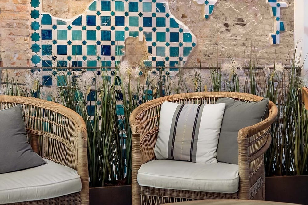 dos sillas de mimbre con almohadas frente a una pared de azulejos