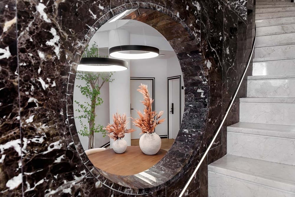 un espejo ovalado en una pared de mármol con jarrones de flores en la mesa