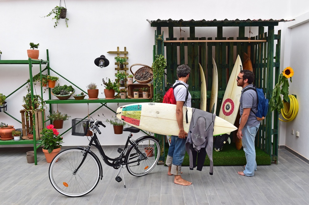dois homens carregam pranchas de surf em frente a uma bicicleta