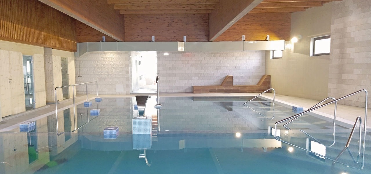 a large indoor swimming pool with a wooden ceiling and stairs leading to it .