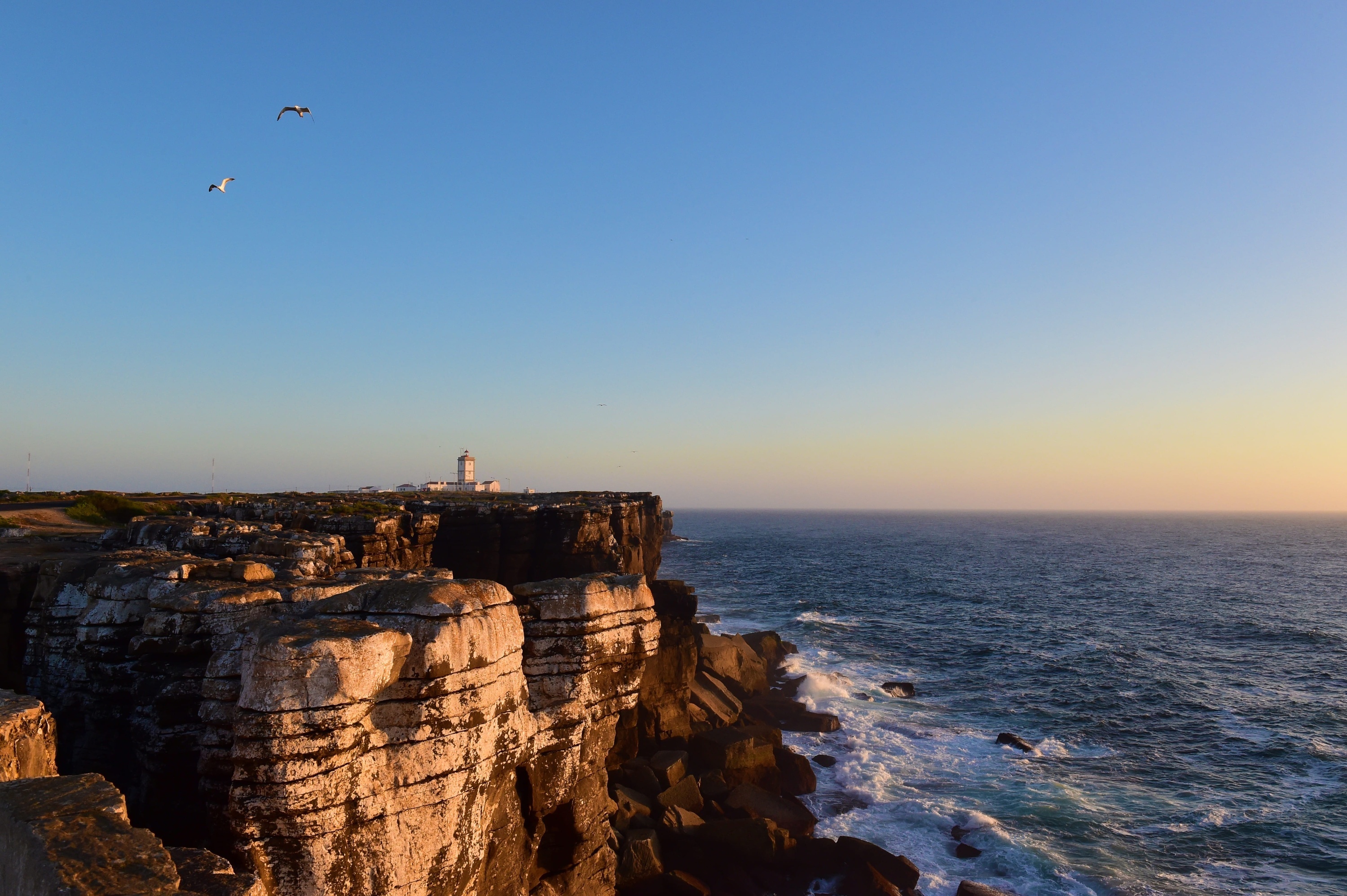 a lighthouse on top of a cliff overlooking the ocean at sunset .