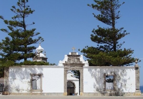 a white building with a cross on top of it is surrounded by trees .