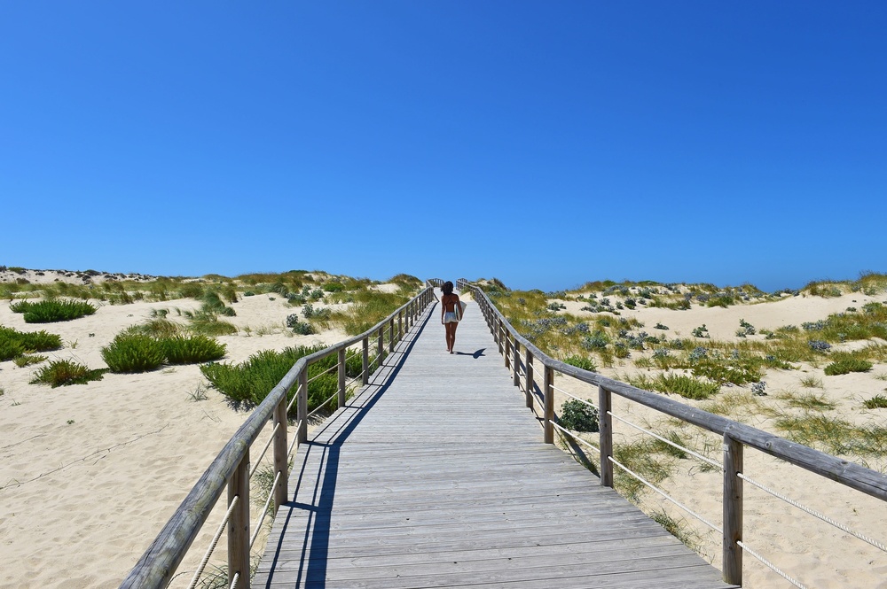 uma mulher caminha por uma passarela de madeira para a praia