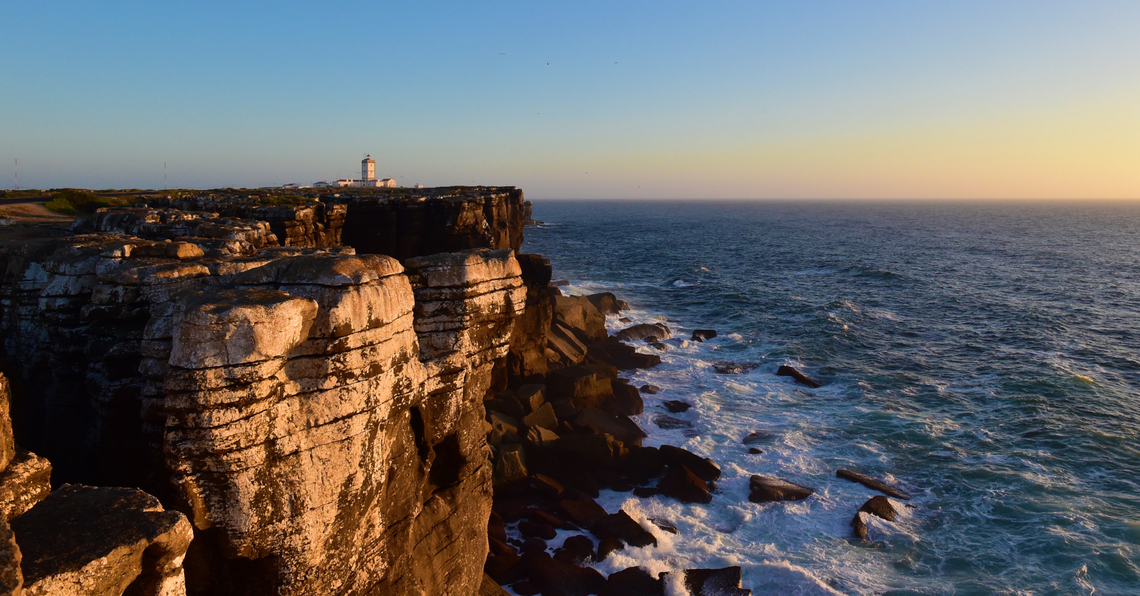 um farol ao lado de um penhasco com vista para o oceano