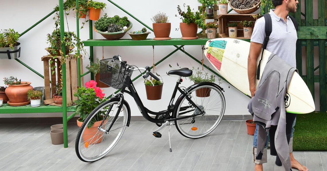 um homem carrega uma prancha de surf ao lado de uma bicicleta