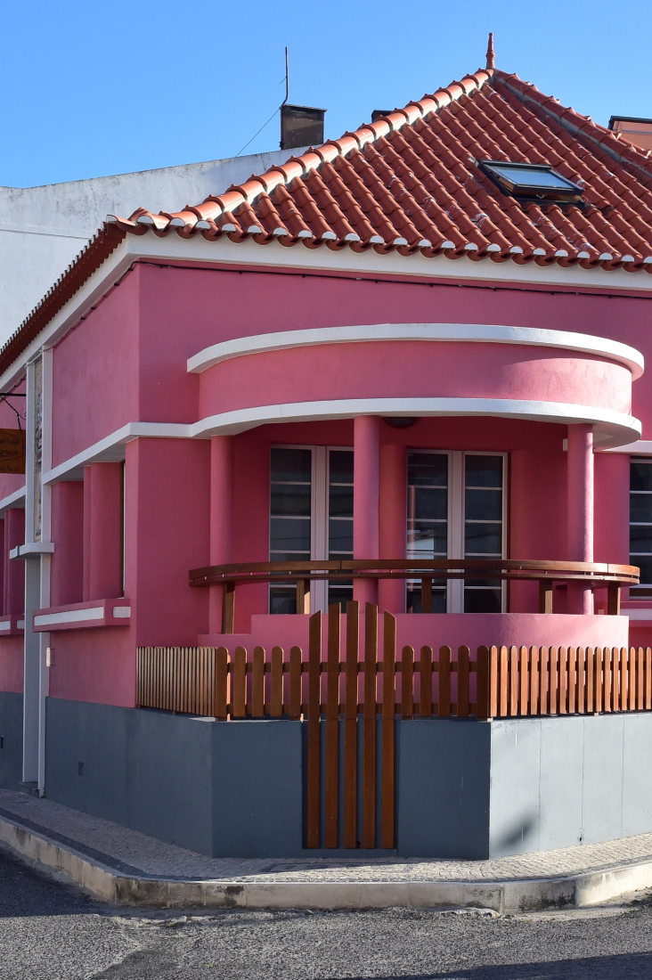 uma casa rosa com um telhado vermelho e uma cerca de madeira