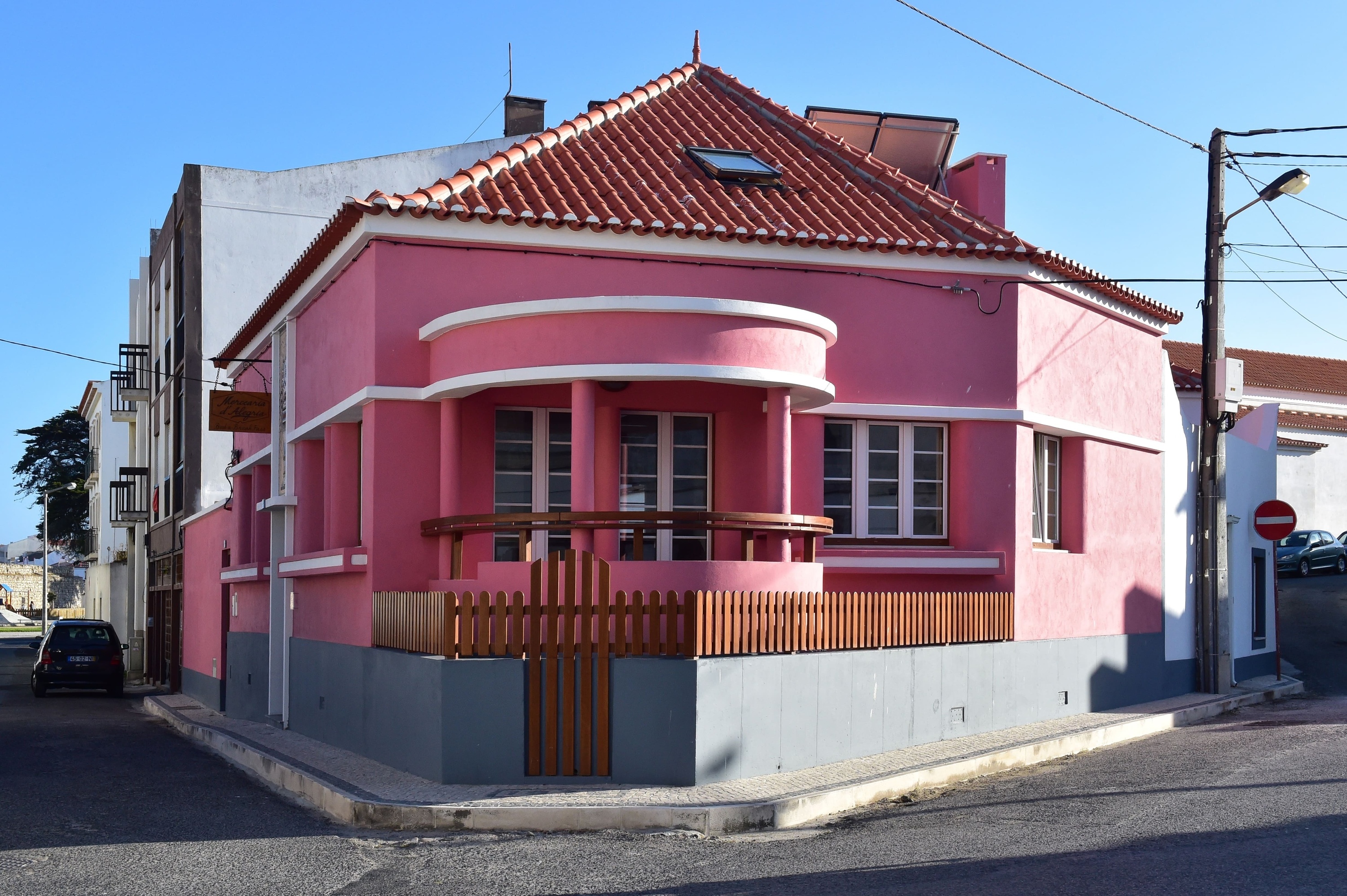 uma casa rosa com um telhado vermelho está na esquina de uma rua