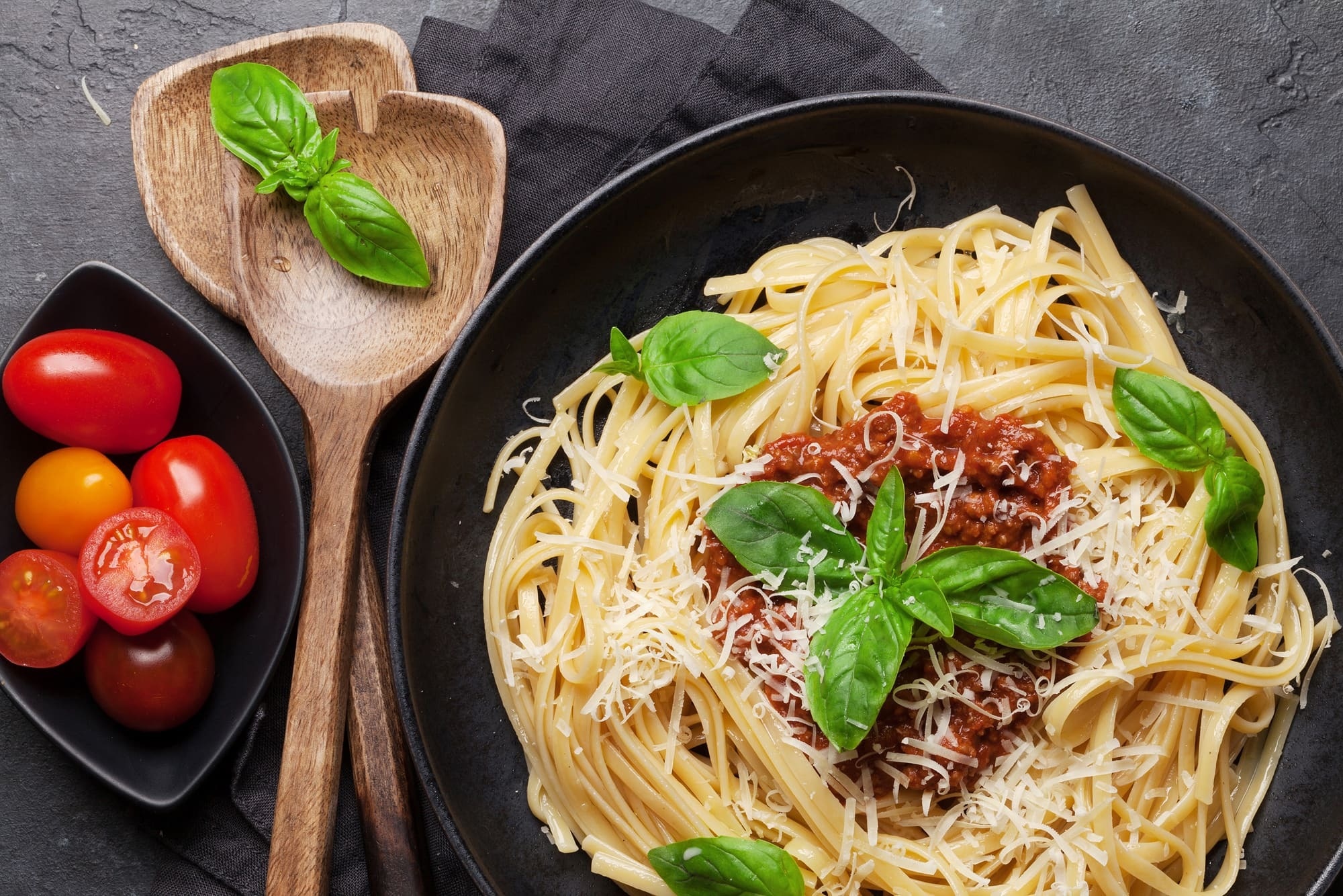 a bowl of spaghetti with meat sauce and basil next to a bowl of tomatoes