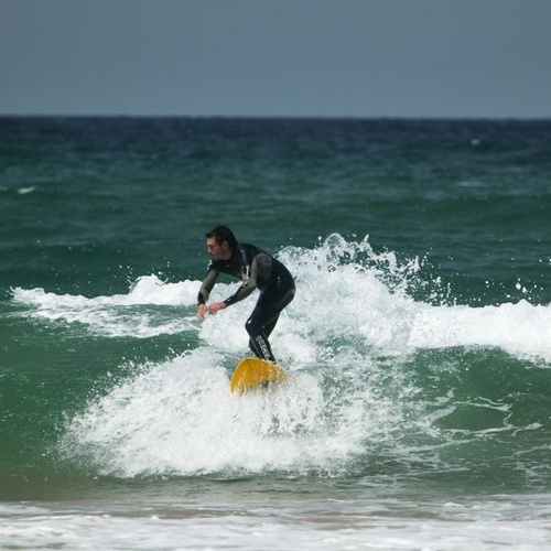 un hombre en traje de neopreno monta una tabla de surf en el océano