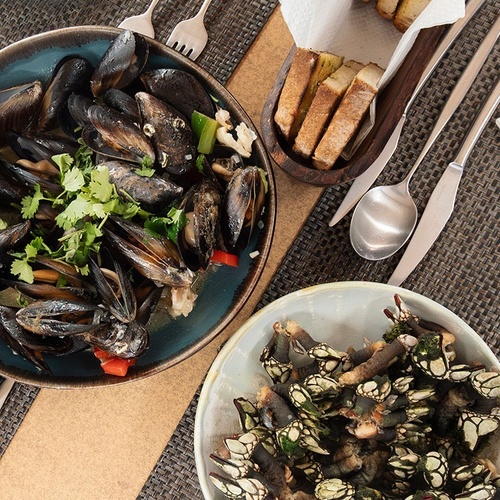 a bowl of mussels sits on a table next to a bowl of crabs