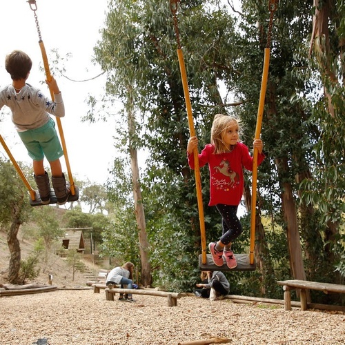 un niño y una niña juegan en columpios en un parque