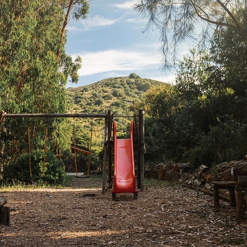a playground with a red slide and swings in the woods