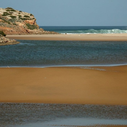 una playa con un río que fluye hacia el océano