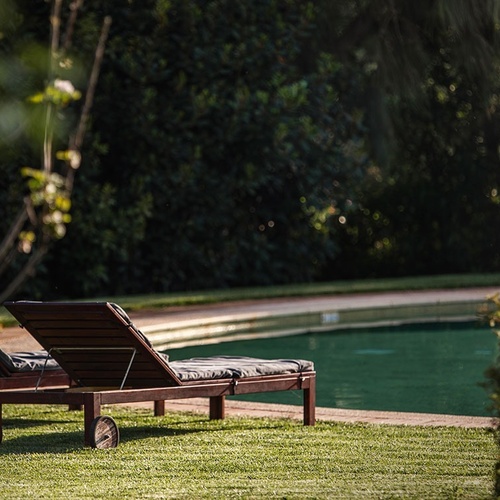 two wooden lounge chairs sit near a swimming pool