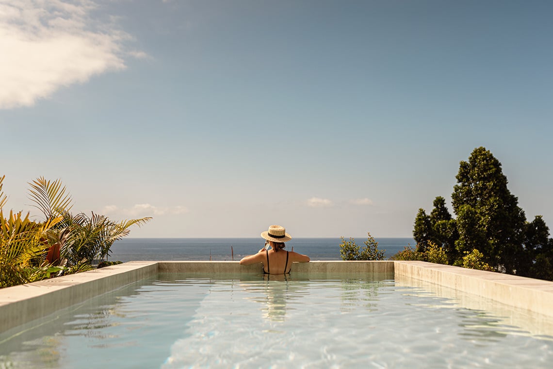Woman in hat relaxes in infinity pool with ocean view - Moon & Sun: Corpo