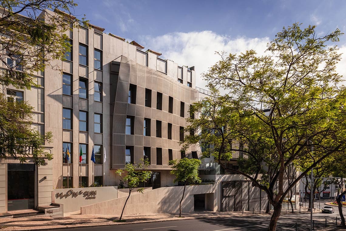 Modern hotel exterior with a textured facade and lush trees. Moon & Sun: Corpo