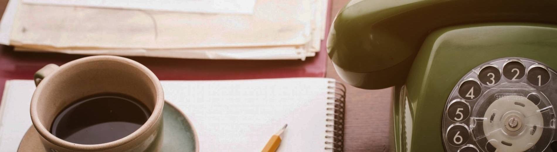 un teléfono verde está sobre una mesa junto a una taza de café y un cuaderno