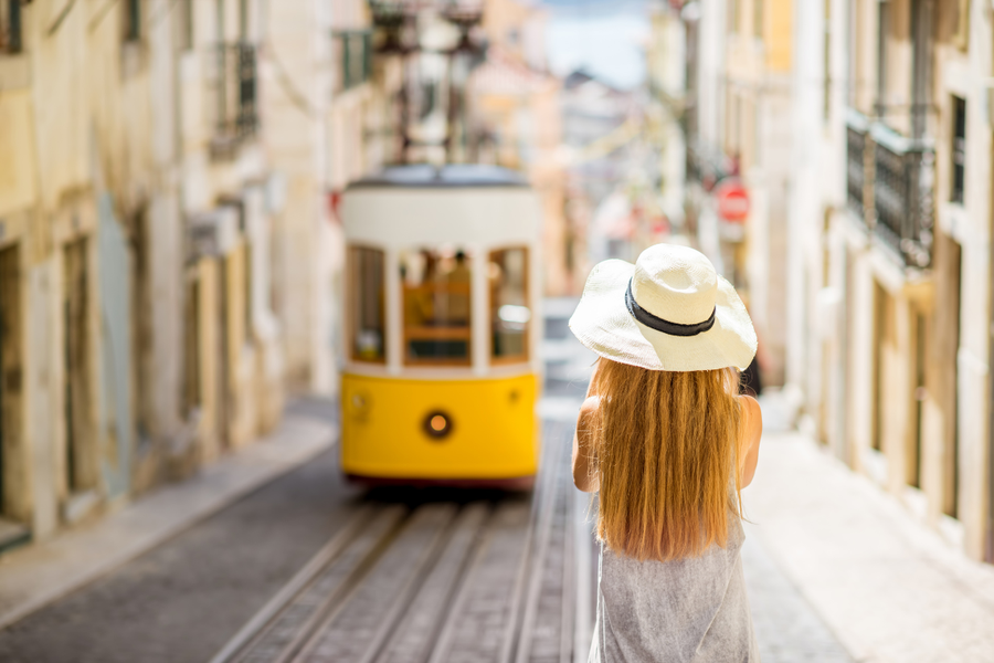 a woman in a hat stands in front of a yellow trolley