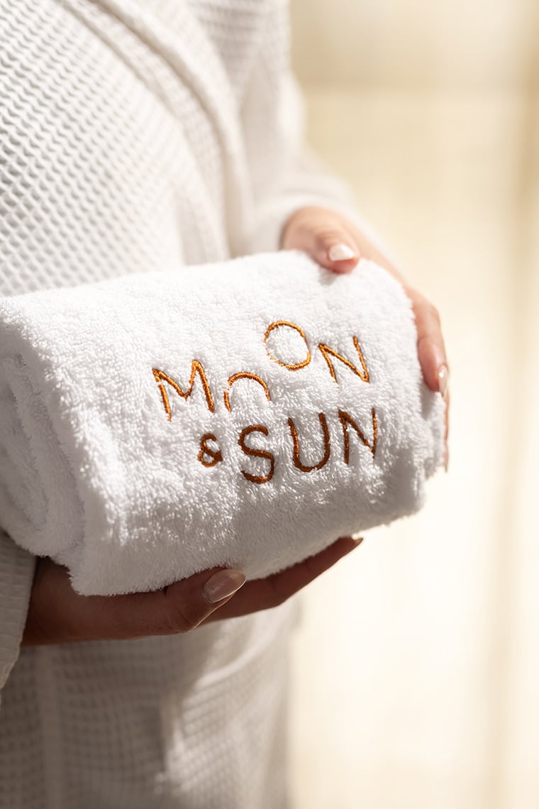 White embroidered towel with 'Moon & Sun' on a hotel guest's robe Moon & Sun: Corpo