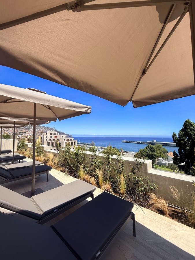Lounge chairs under Moon & Sun umbrellas with ocean views and a townscape.