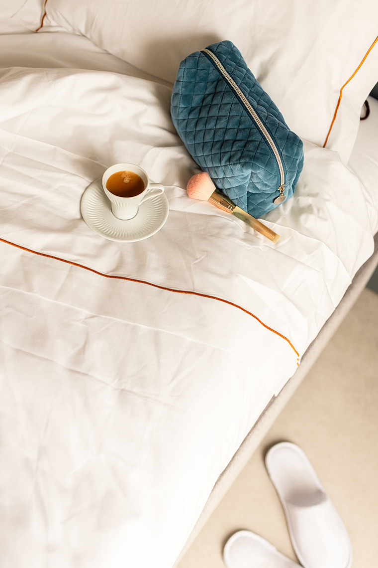 Luxury hotel room with espresso, makeup bag, and slippers on white bedding. Moon & Sun: Corpo