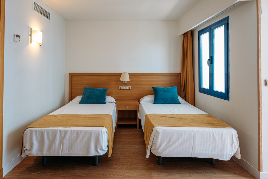 Habitación de hotel con dos camas individuales, ropa de cama blanca, cojines azules y MS hoteles: Puerto Marina.