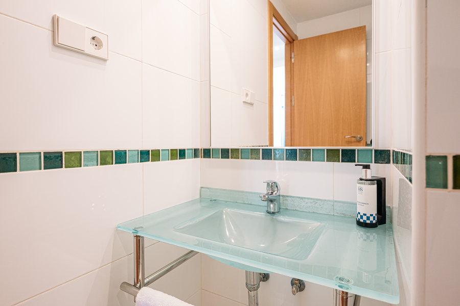 Espejo sobre lavabo de cristal con dispensador de jabón y enchufe en baño de hotel. MS hoteles: Puerto Marina