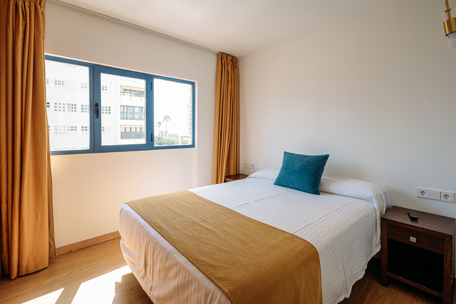 Habitación de hotel con cama, ventana y cortinas ocres. MS hoteles: Puerto Marina acogedor.